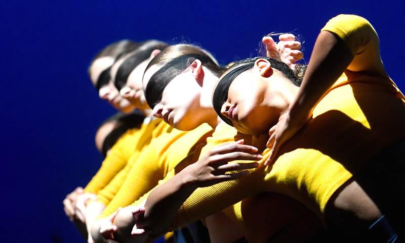 Group of four female dancers in a dramatic pose wearing a black cloth mask